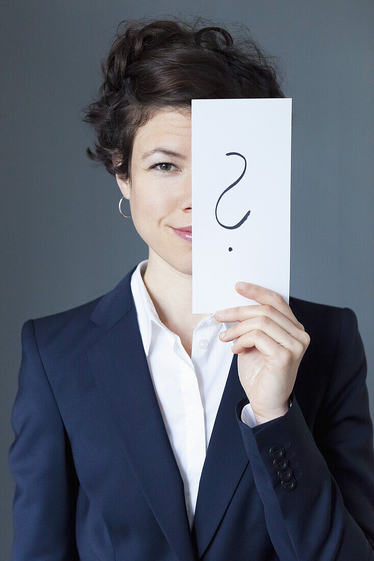Smiling mid adult woman holding paper with question mark, close-up