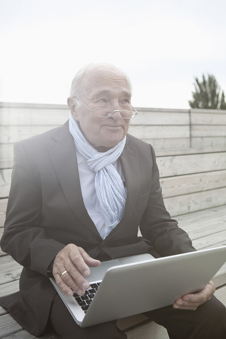 Senior man holding laptop, looking away