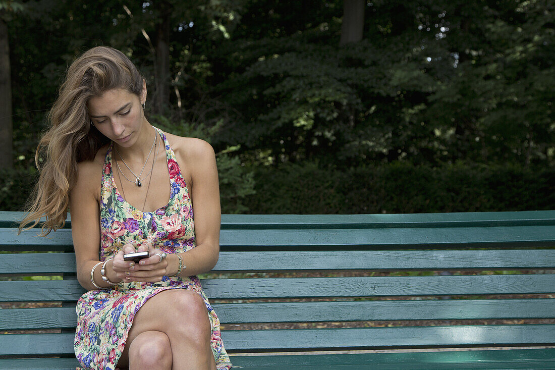 Young woman sitting on park bench using mobile phone