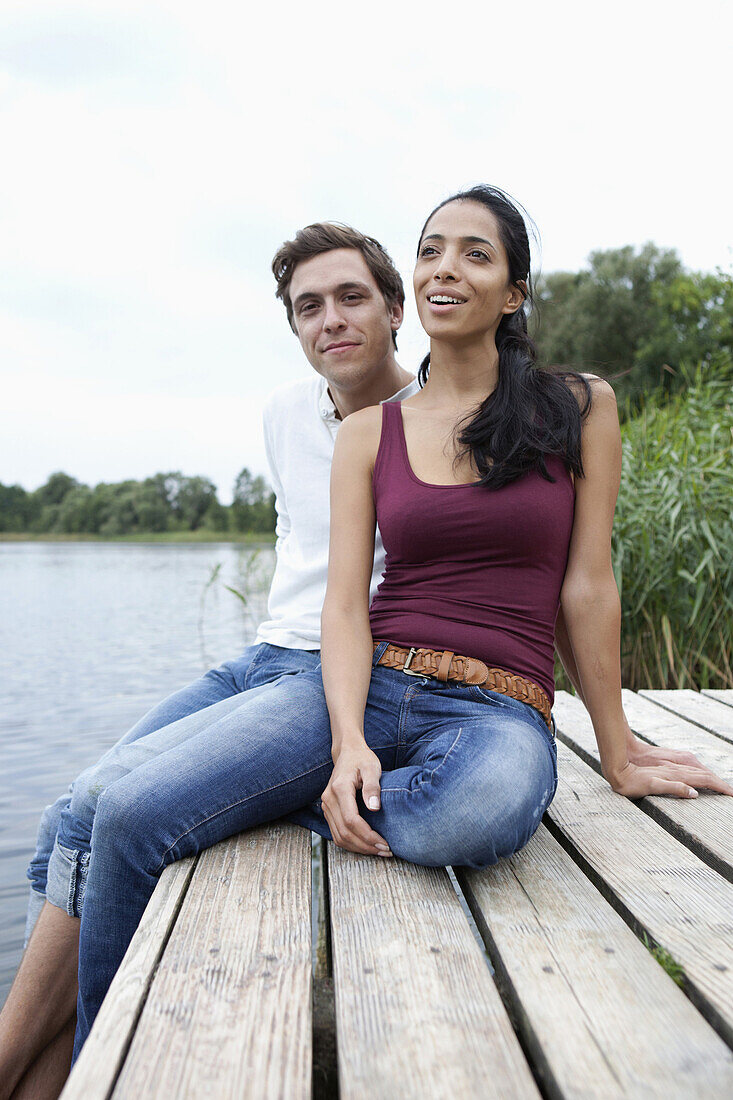 Young couple sitting on wooden pier, smiling
