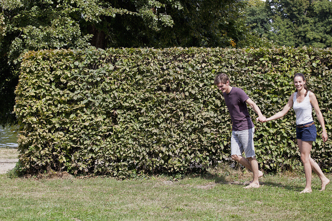 Young couple holding hands and walking by hedge
