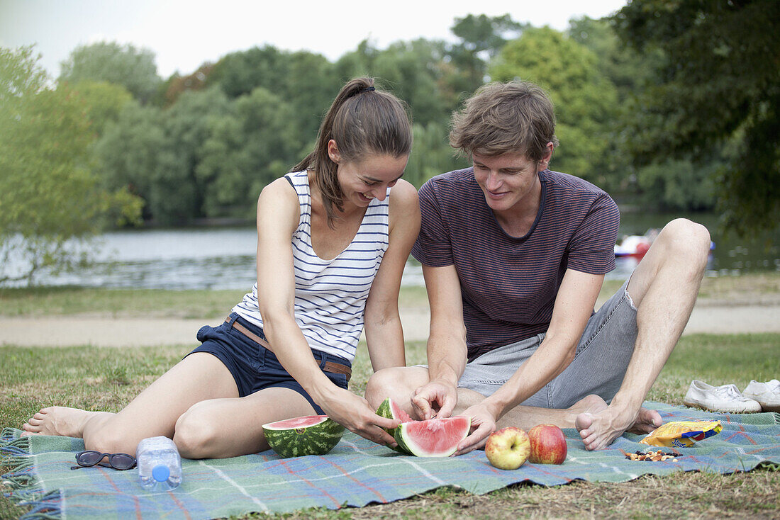 Young couple having picnic, cutting watermelon