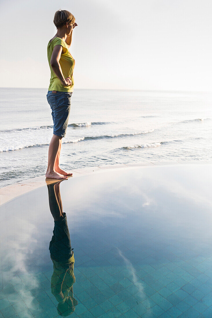Woman standing on a wall of an infinity pool over Indian Ocean, Amed, Bali, Indonesia