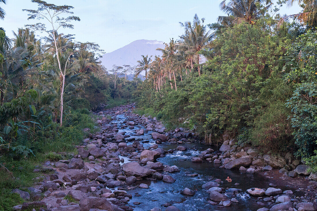 Mann badet in einem Fluss, Gunung Agung im Hintergrund, bei Sidemen, Bali, Indonesien