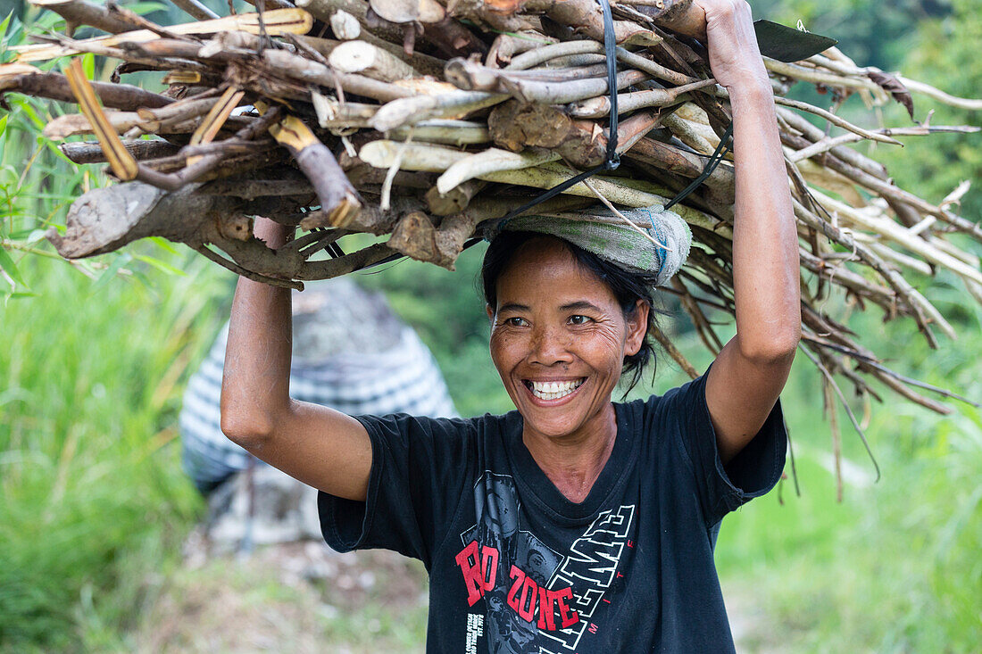 Smiling woman carrying a bunch of wood on her head, near Sidemen, Bali, Indonesia