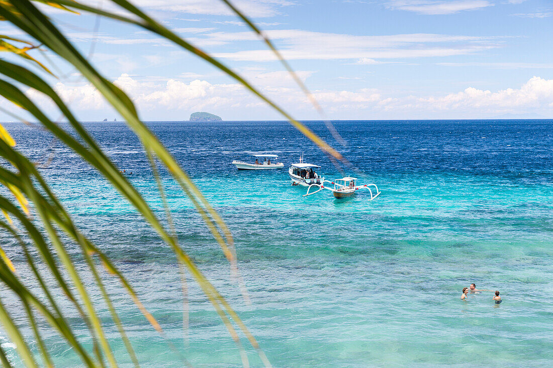 Tourists swimming in blue lagoon, fishing boats in background, Padangbai, Bali, Indonesia