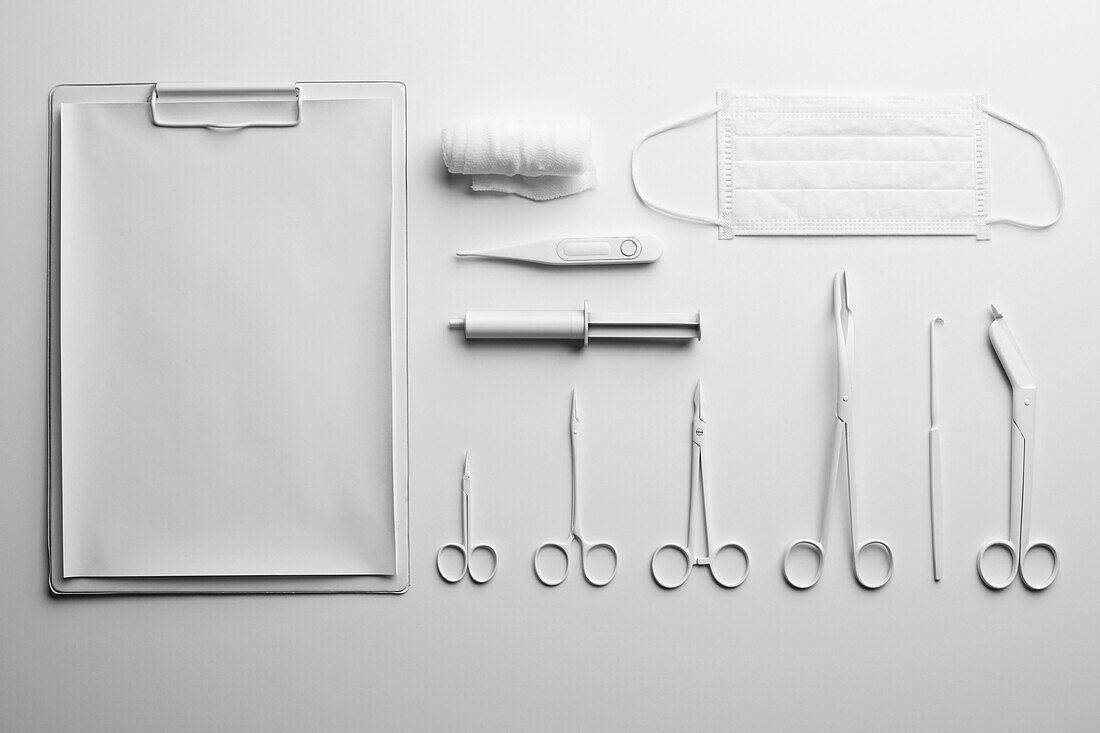 Clipboard, various medical scissors and instruments painted white and arranged neatly