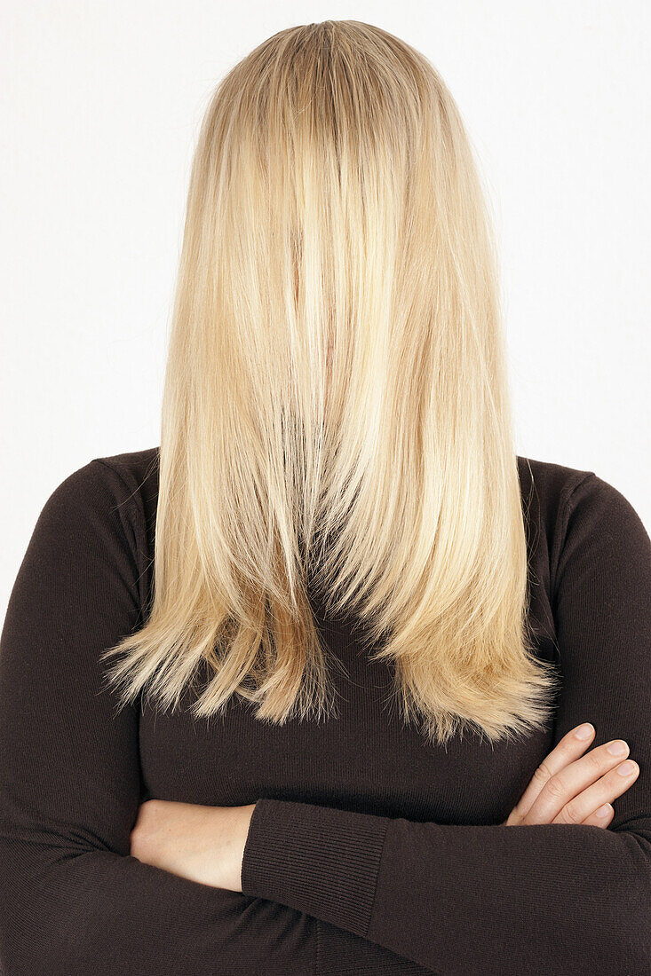 A woman standing with her long, blond hair combed forward covering her face