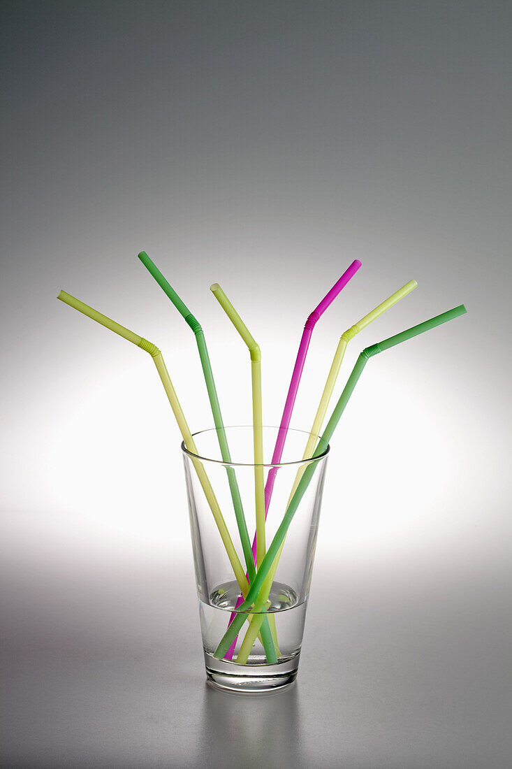 A glass with water in it and three yellow drinking straws, two green ones and one pink one