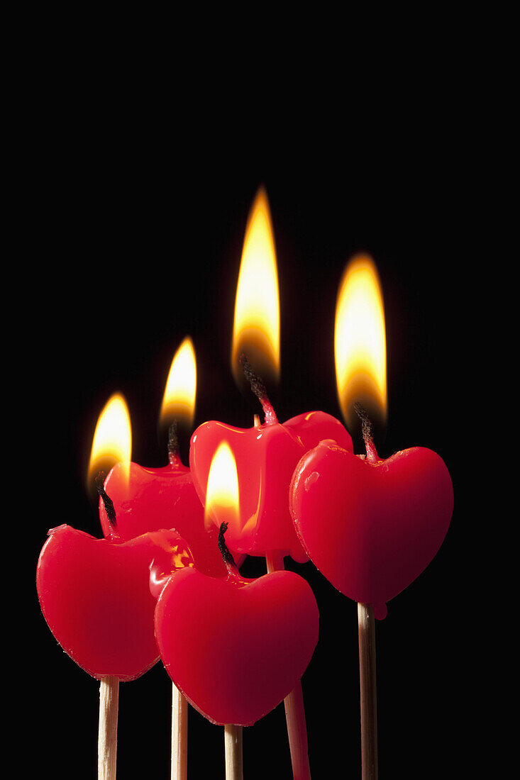 Five lit heart shaped candles on sticks arranged in a group