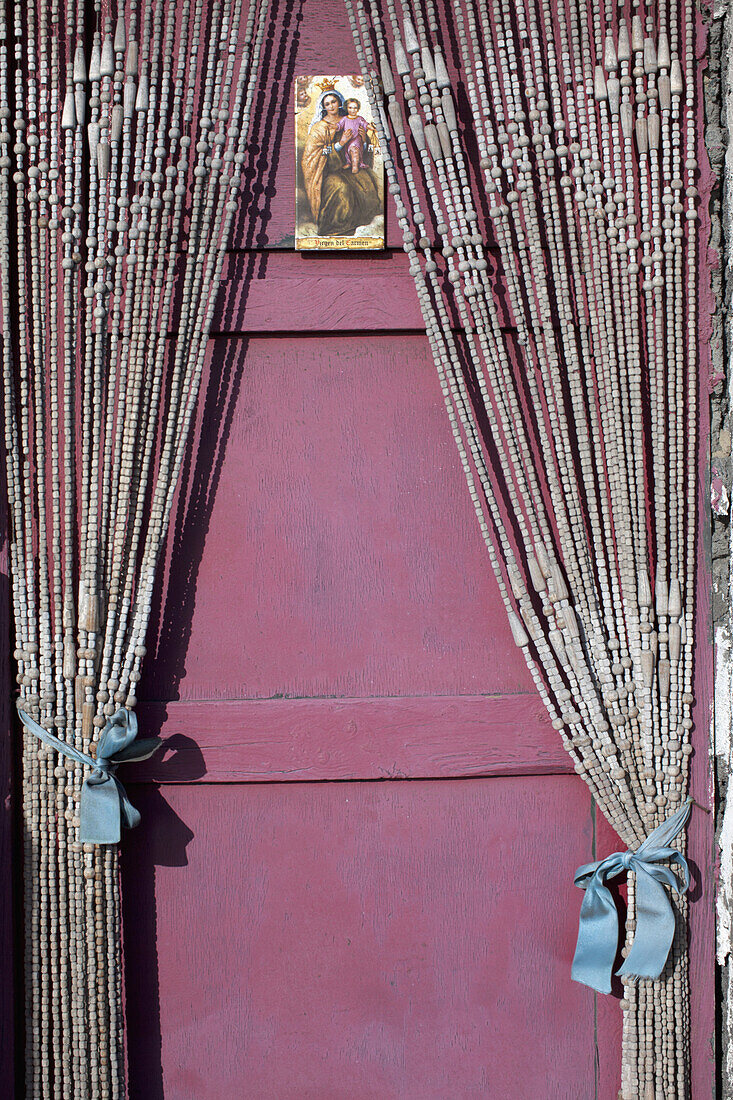 A holy card with the Virgin Mary and the baby Jesus hanging on a door with beaded curtains