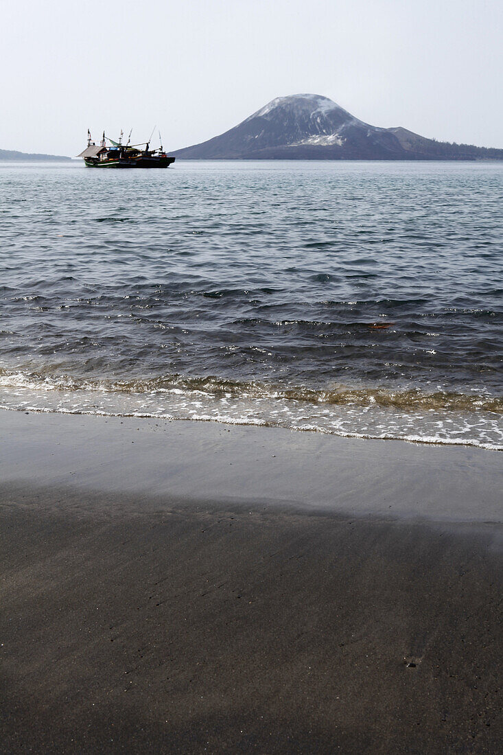 Water's edge, view of boat moving past Krakatau volcano, Indonesia