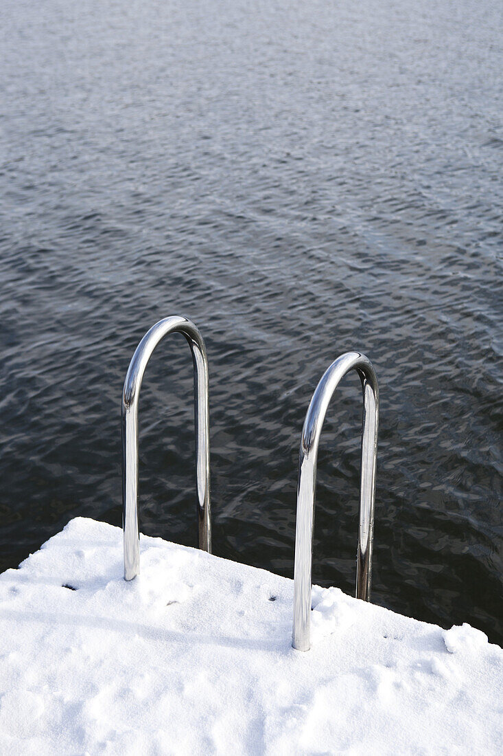 A snow covered dock with a ladder going into rippled water