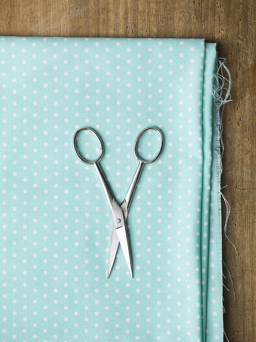 A pair of scissors on top of polka dotted fabric
