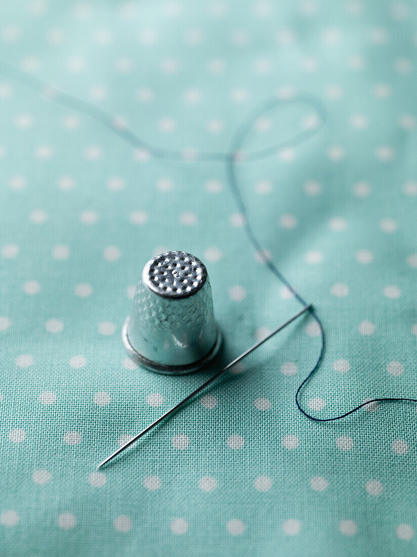 A threaded needle and thimble on top of polka dotted fabric