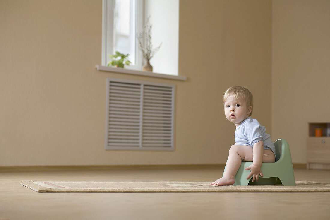 A toddler sitting on a potty chair, looking at camera