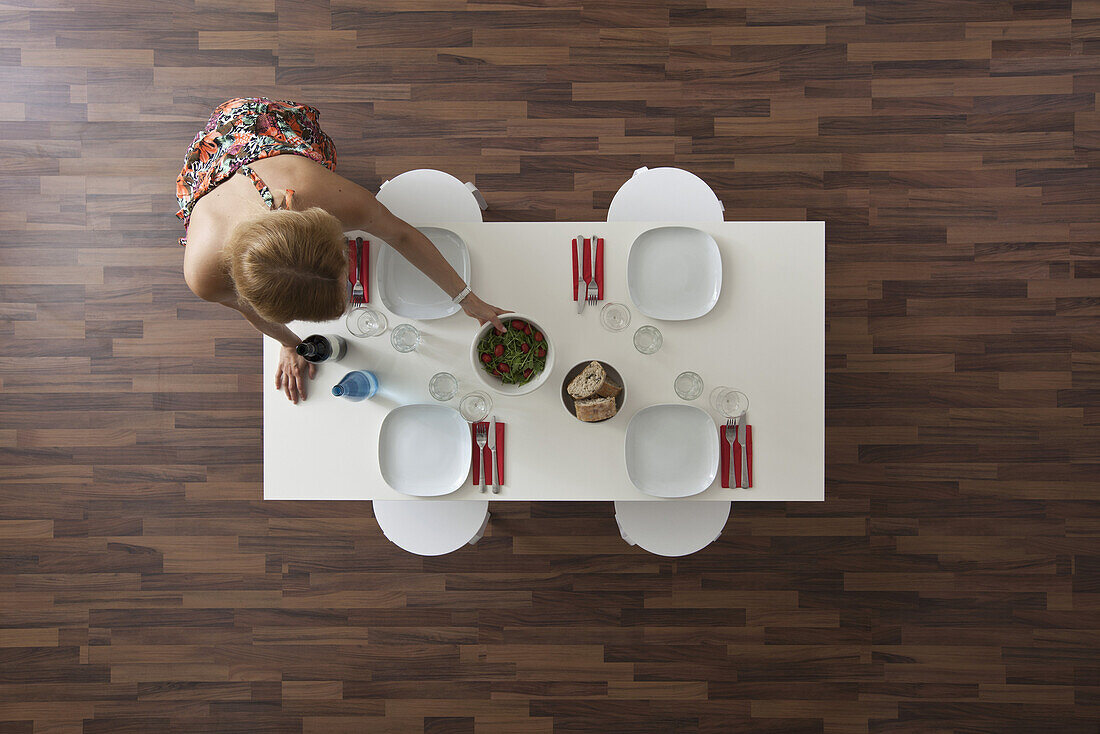 Woman setting dining room table for dinner party, overhead view