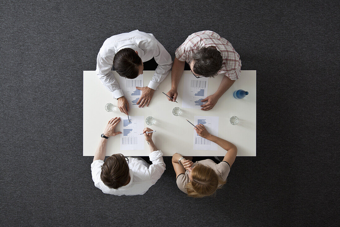 A business meeting with three businessmen and a businesswoman, overhead view