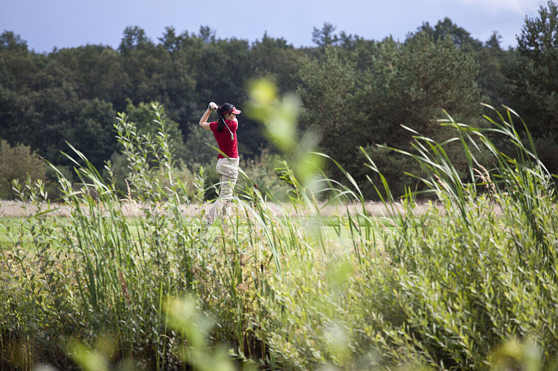 A female golfer teeing off, focus on background