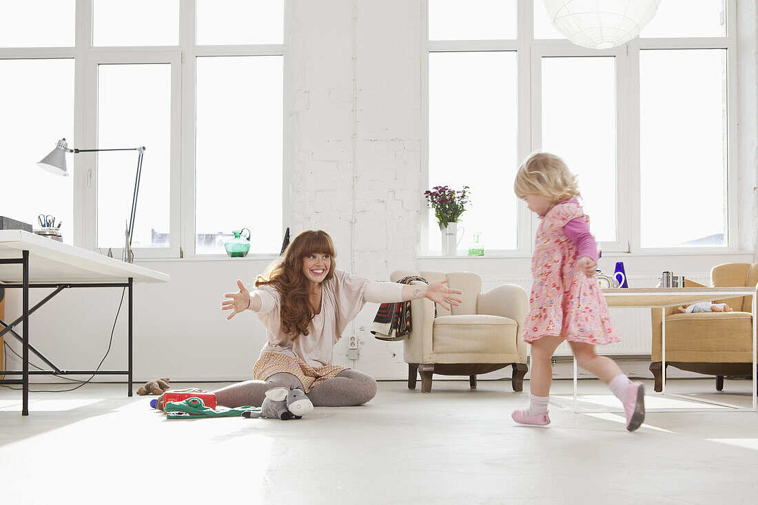 A young girl running towards her mother sitting on the floor