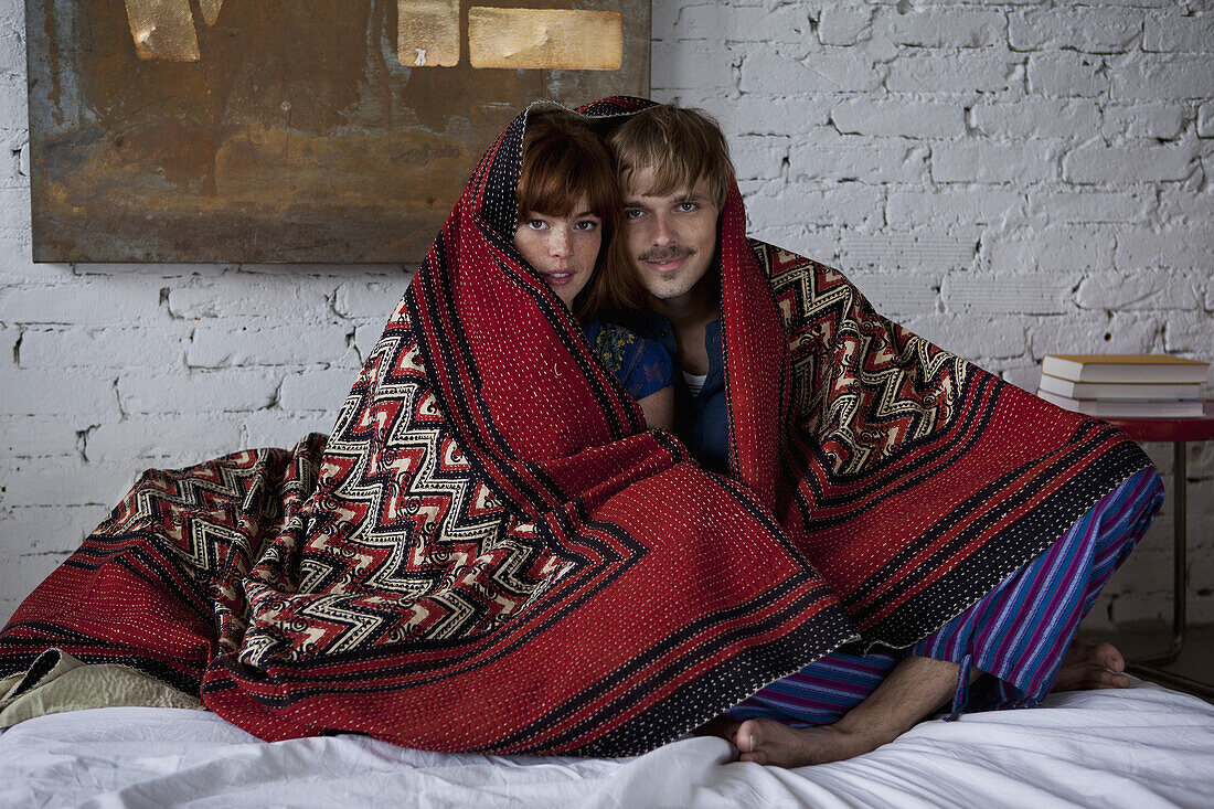 A serene couple wrapped in a blanket sitting on a bed