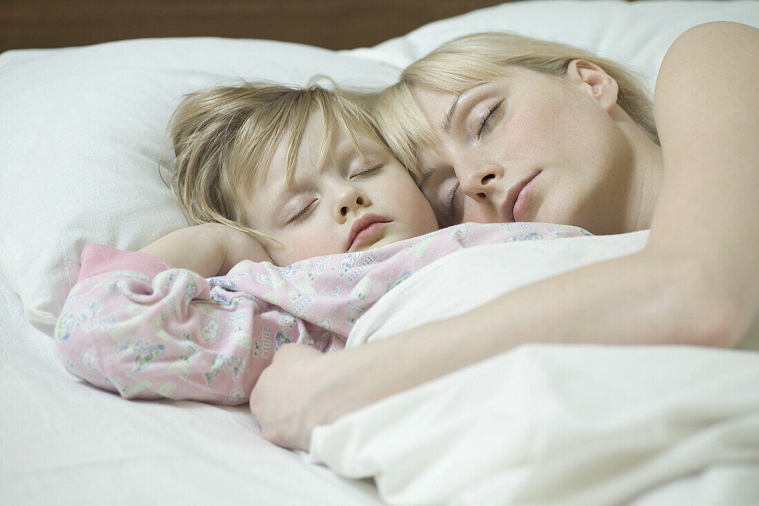 A mother and her young daughter sleeping a bed side by side
