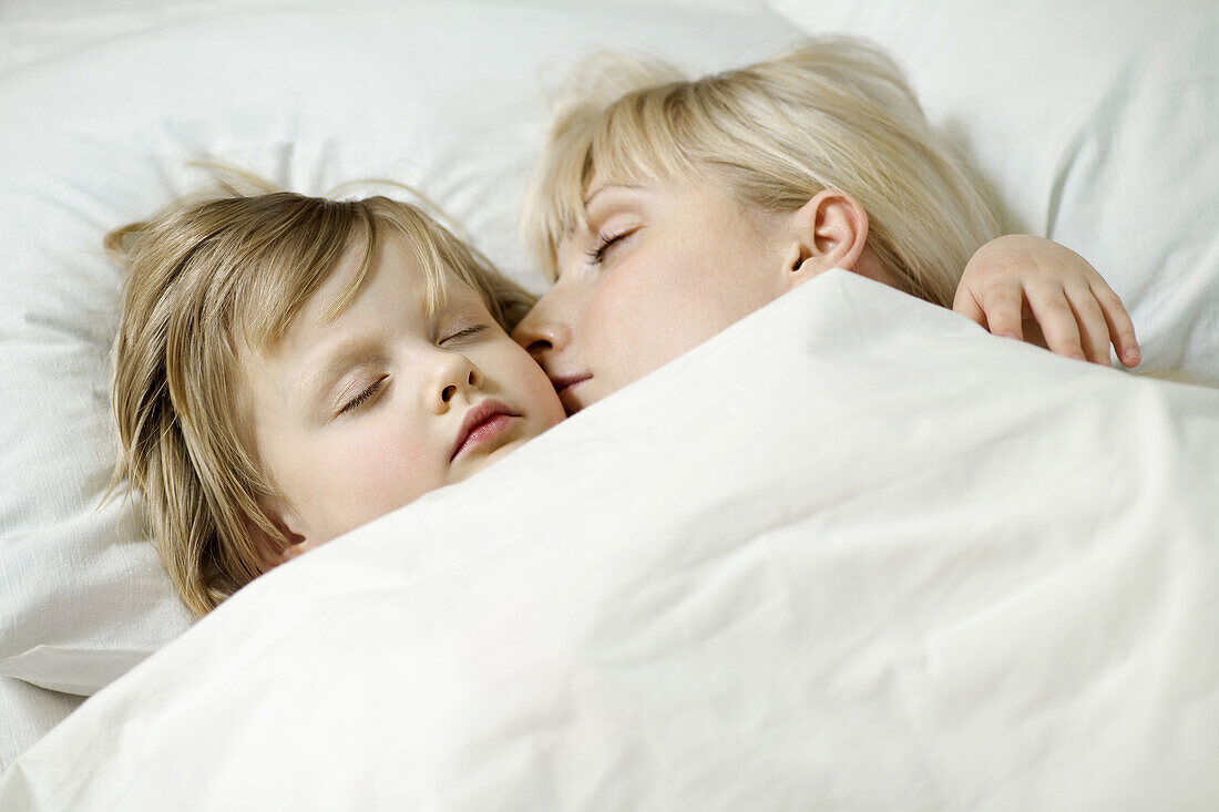 A mother and her young daughter sleeping a bed side by side