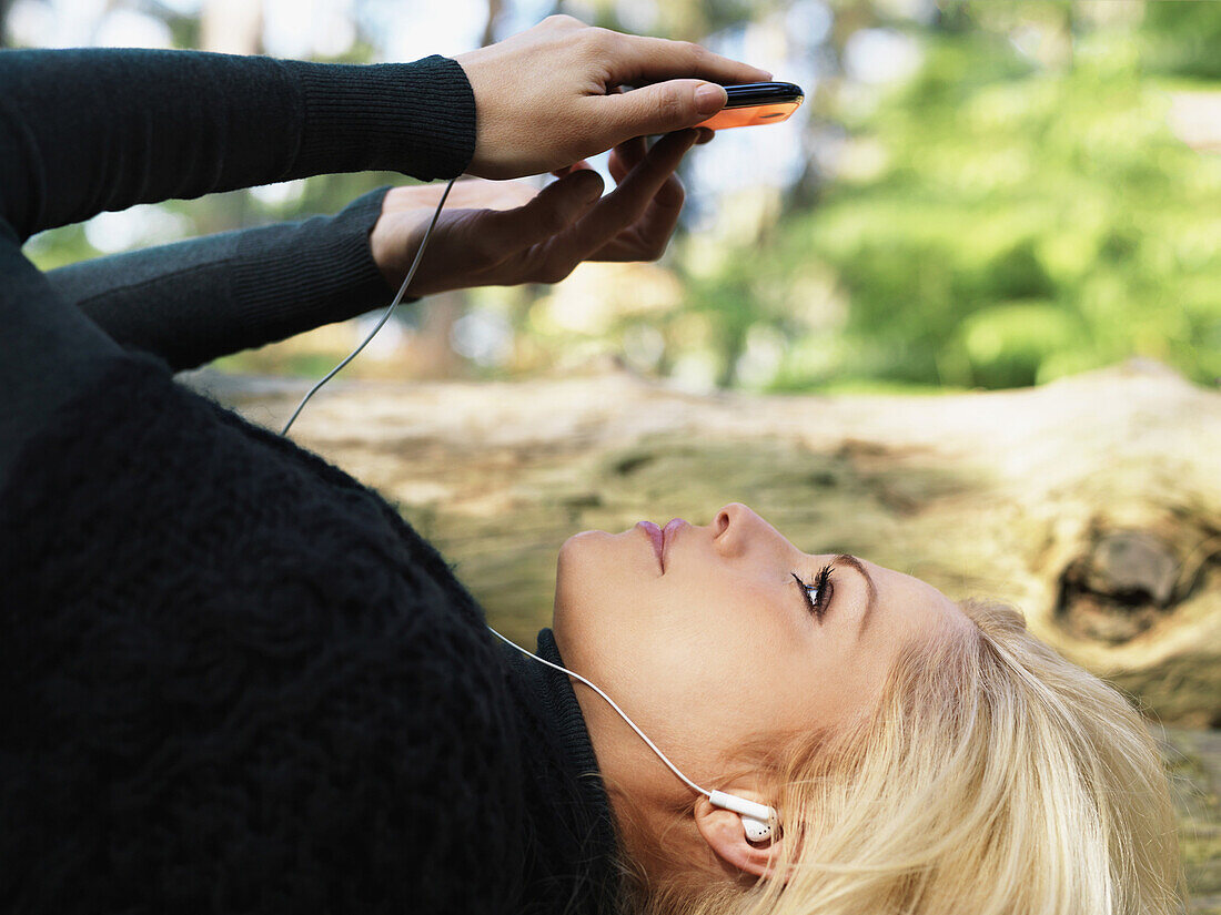 A woman wearing earphones and using a smart phone, outdoors