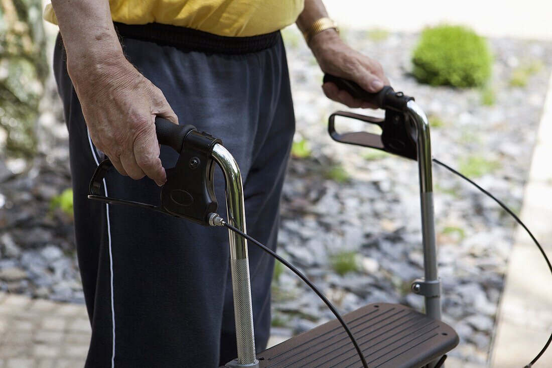 A senior man standing with a walker, midsection, outdoors
