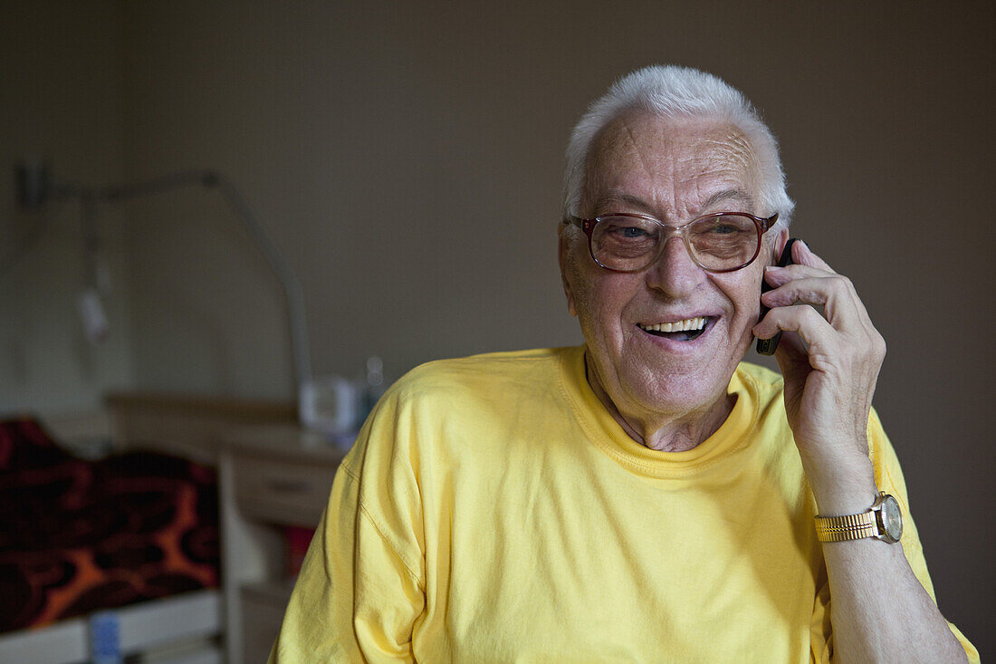 A cheerful senior man living in a nursing home, using a mobile phone