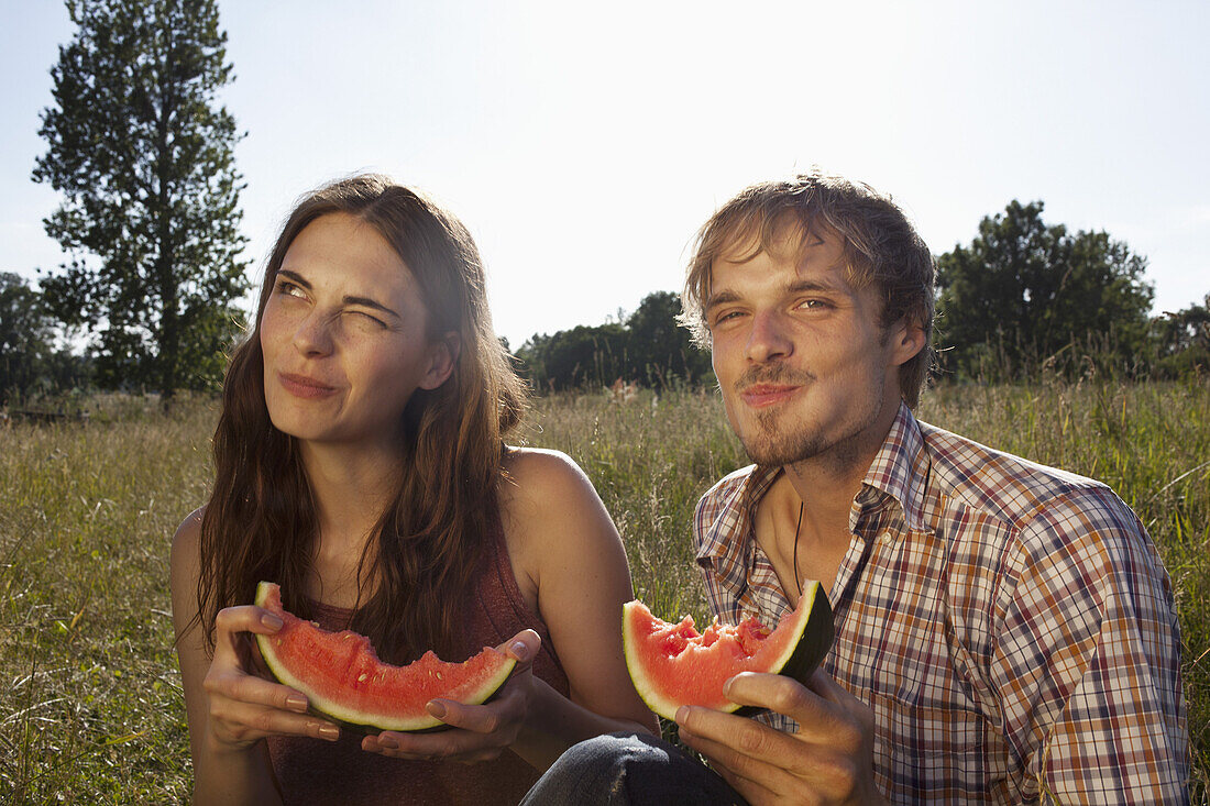 Couple sitting eating melon in field