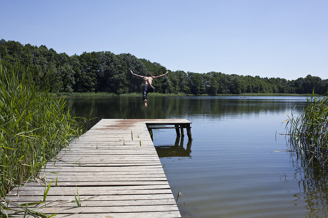 Guy on jetty dives into lake with arms outstretched