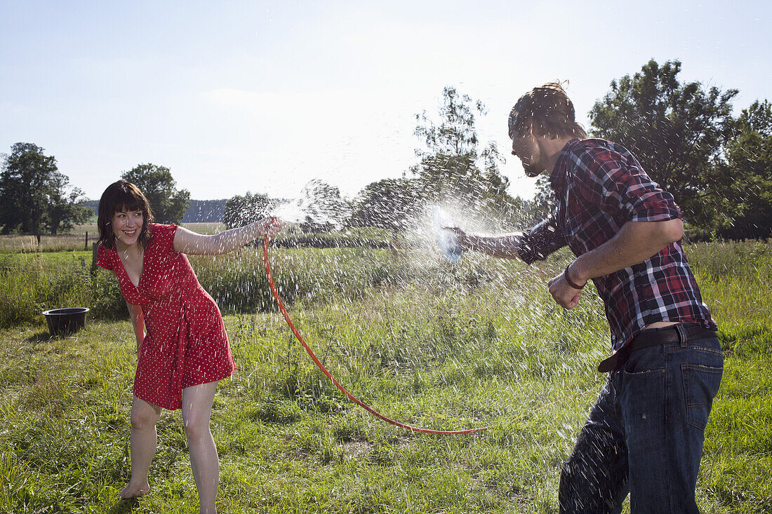 Man and woman spray each other with water in field