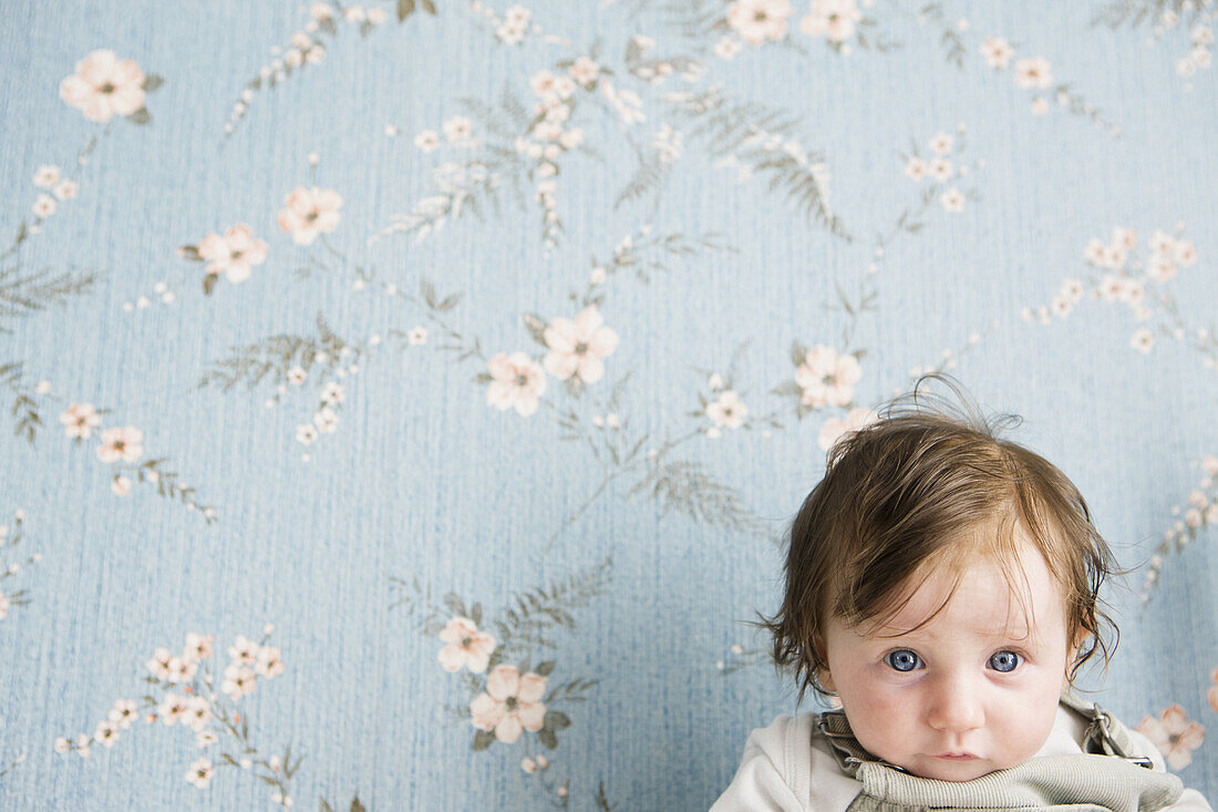 Portrait of a baby in front of floral wallpaper