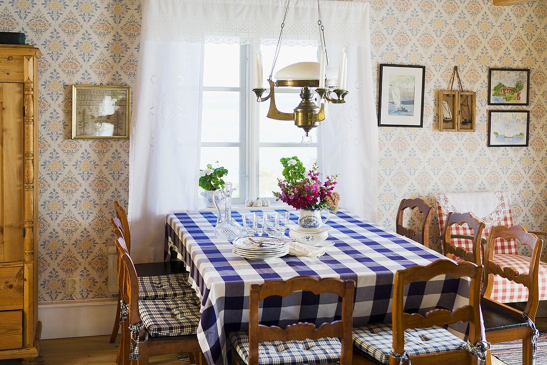 A cosy country dining room with a dining table with a checked table cloth in front of a window