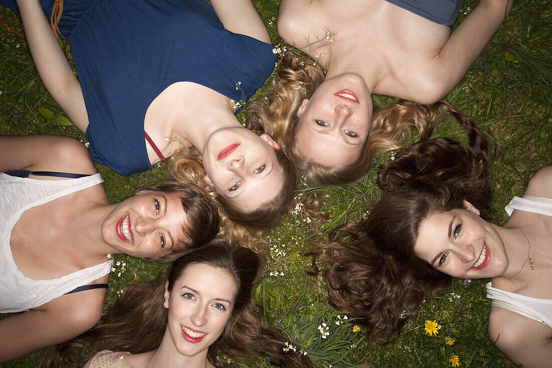 Five cheerful female friends lying in the grass, head and shoulders