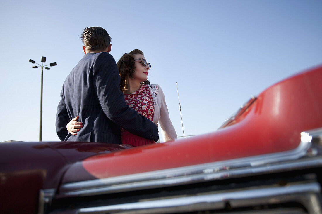 A cool, rockabilly couple with arms around each other by a vintage car