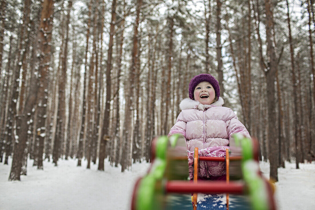 A young cheerful girl on a piece of playground equipment in winter