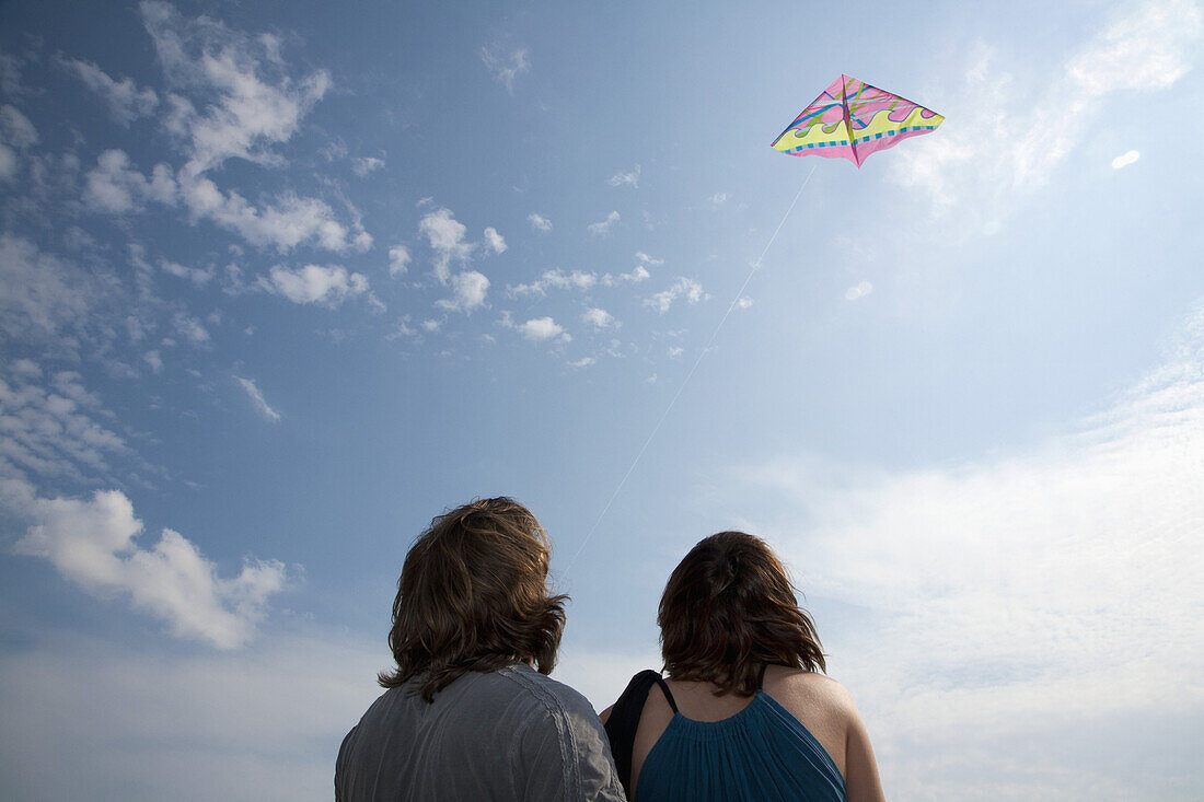 A young couple flying a kite, rear view