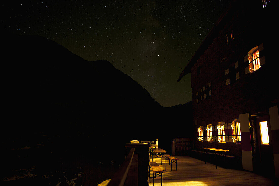An illuminated building against a silhouetted mountain and starry sky