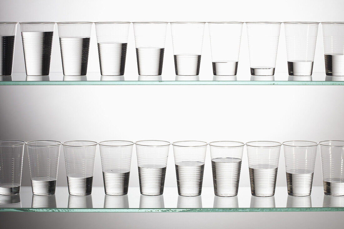 Two shelves with glasses of water filled with varying amounts of water