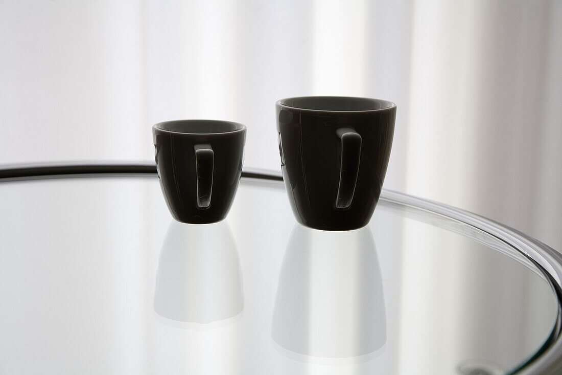 A coffee cup and an espresso cup reflected on a glass table