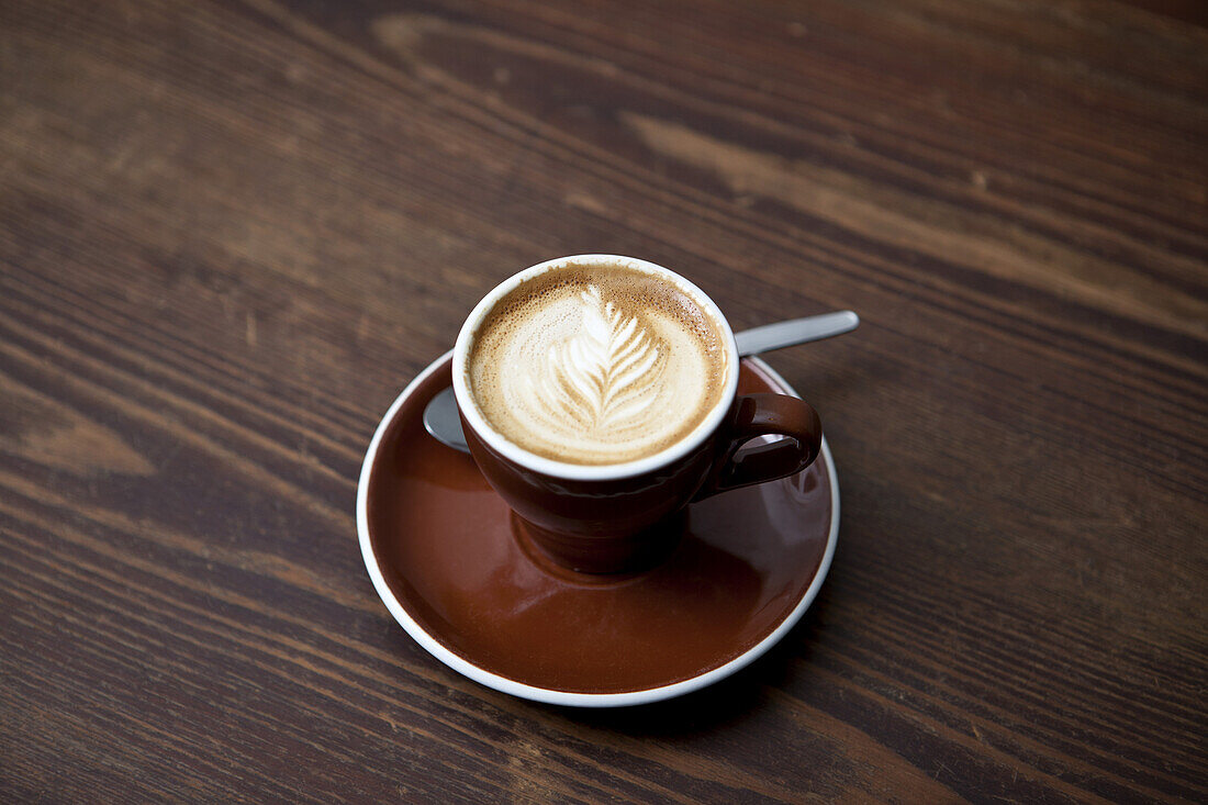 A cafe latte with a floral pattern in the milk froth on a table in a cafe