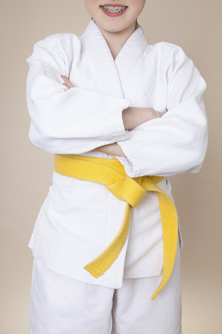 A smiling girl with arms crossed wearing martial arts uniform with yellow belt