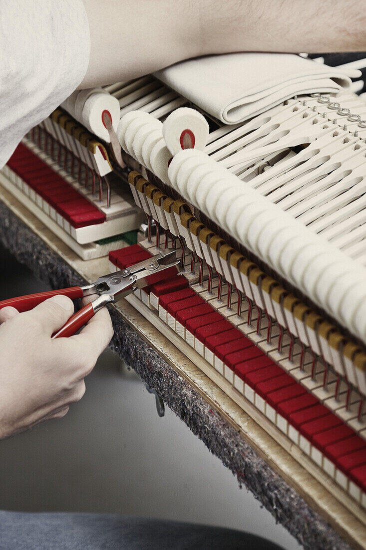 A piano repairman using pliers to fix a piano