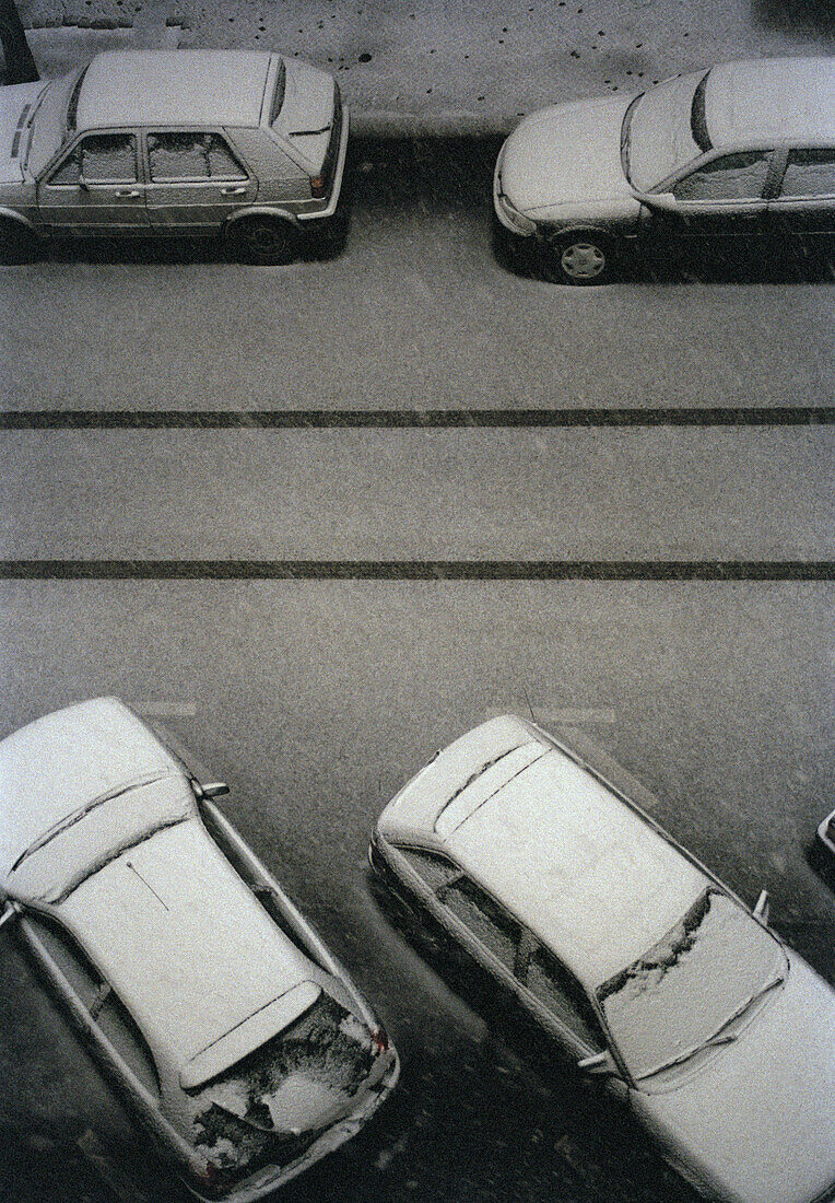 Four cars covered in snow on a street