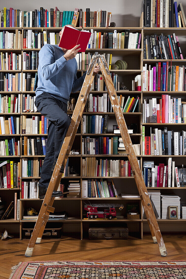 A man reading on a ladder in a home library