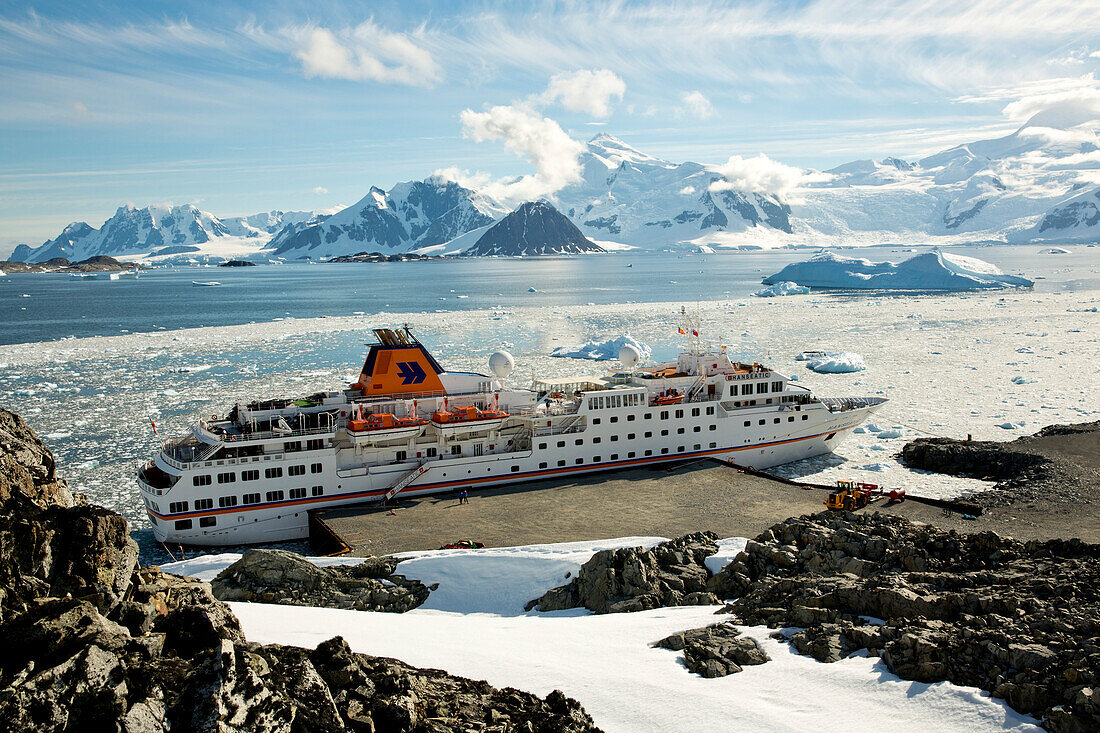 Expedition cruise ship MS Hanseatic (Hapag-Lloyd Cruises) moored at the concrete pier with icebergs and mountains in the distance, Rothera Station, Marguerite Bay, Antarctica