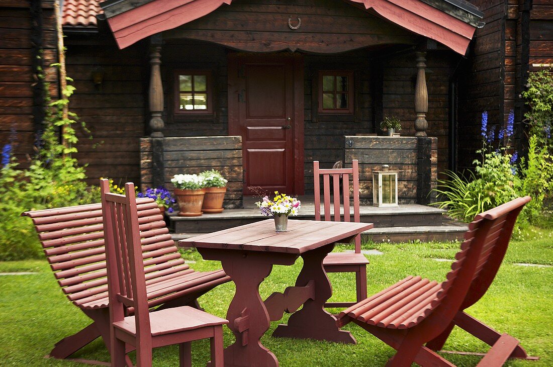 Red garden furniture on a field with an old weekend house with a veranda in the background