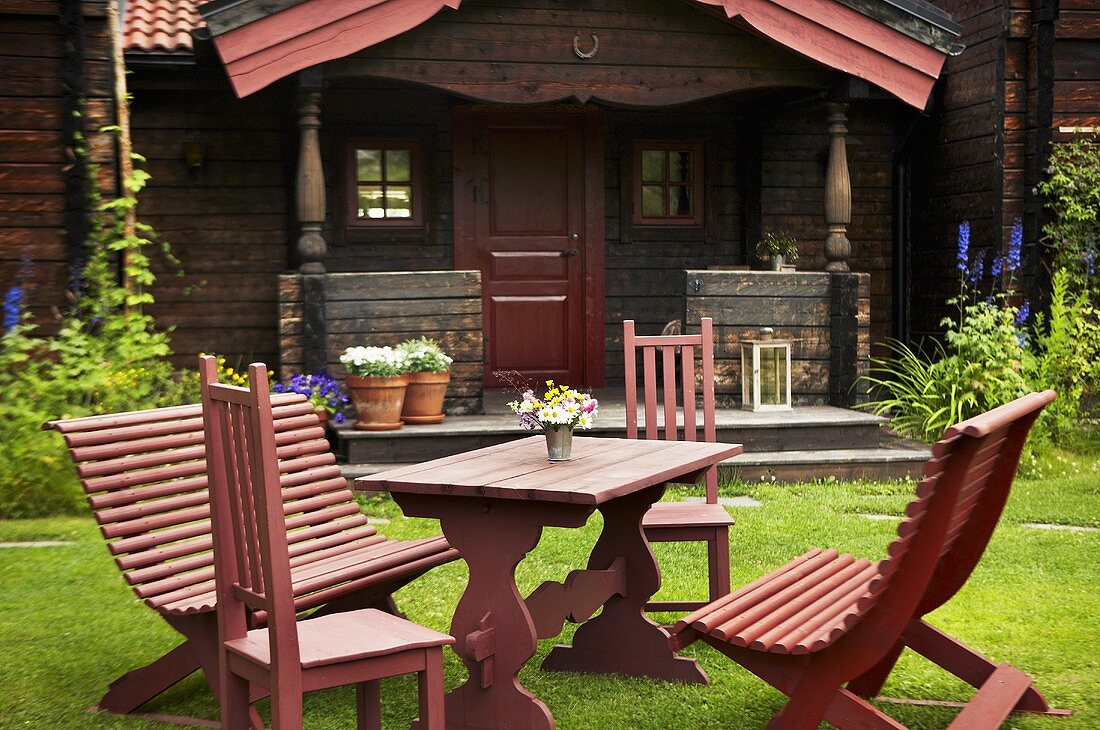 Rote Gartenmöbel in der Wiese vor altem Wochenendhaus mit Veranda